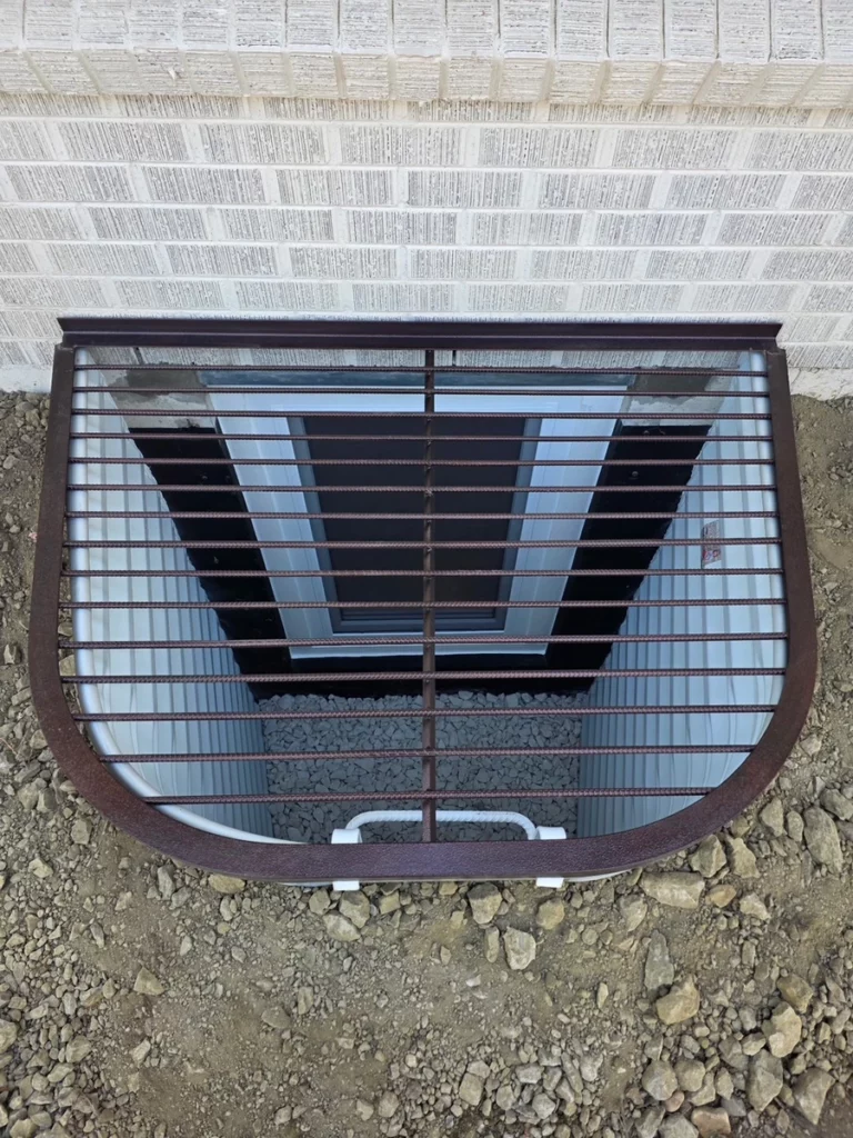 Bronze finish grate covering a galvanized egress window well beside a brick wall in Boulder, CO.