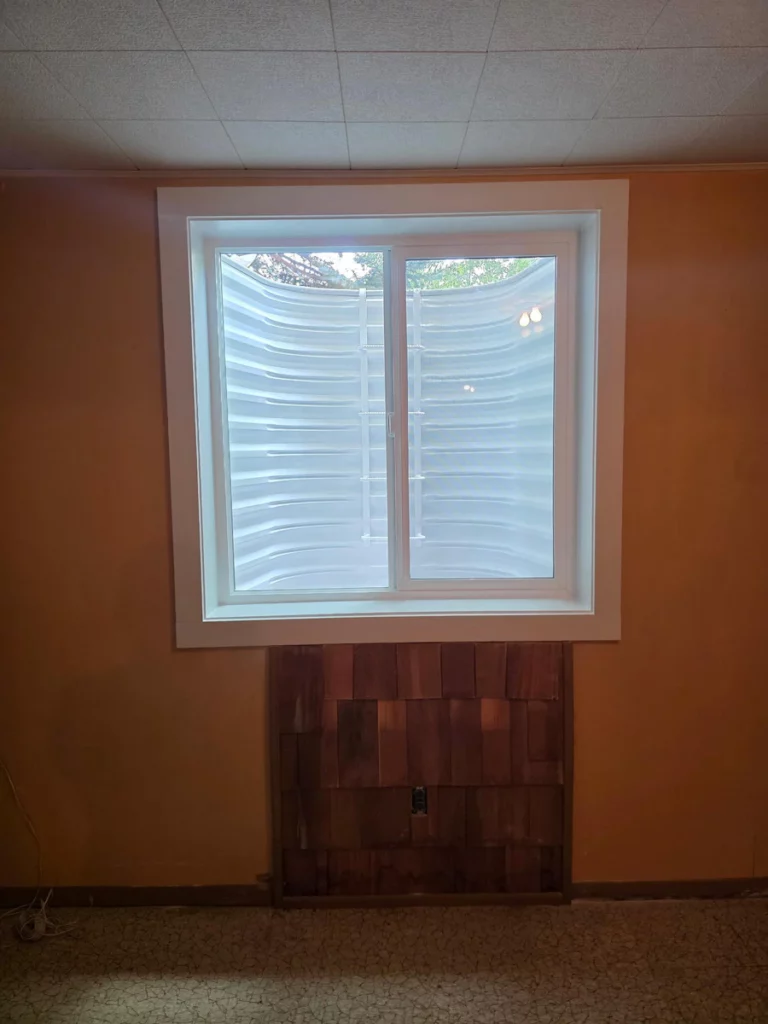 White basement slider with trim above a wood shingle panel, ladder visible in the well, in Lakewood, CO.
