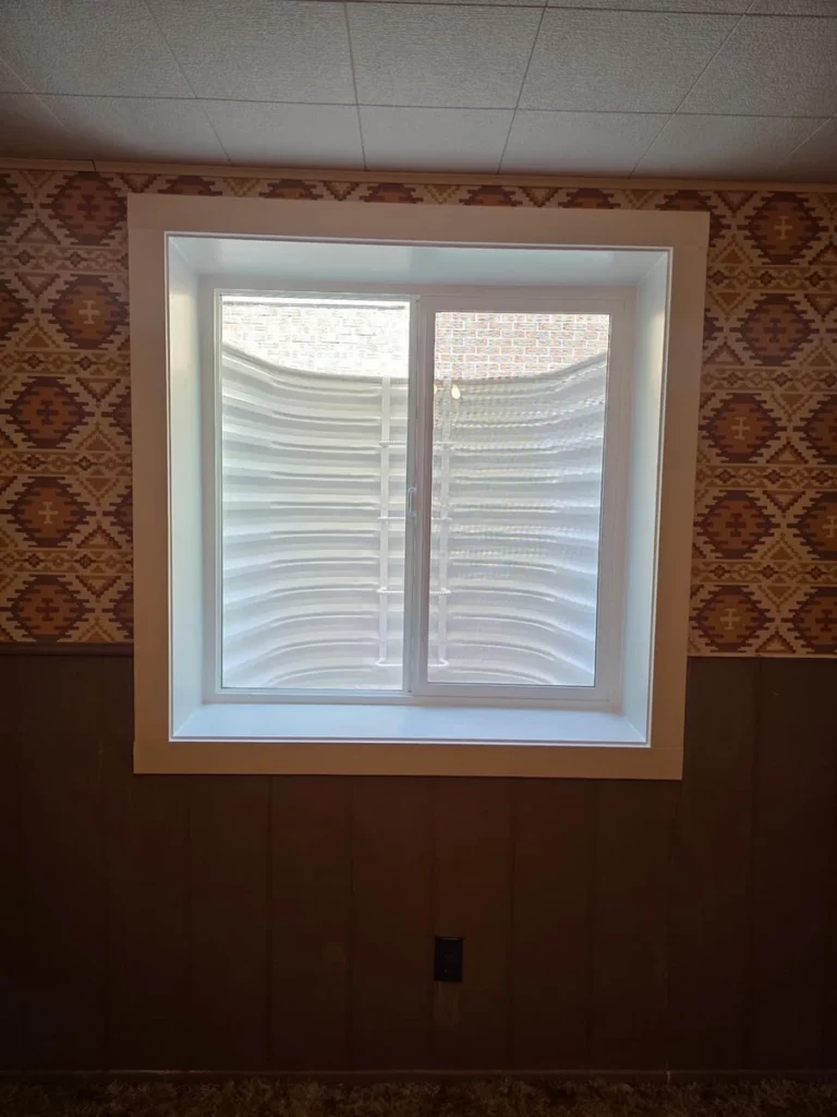 White 48 x 48 slider with new trim against patterned wallpaper and paneling in a basement in Lakewood, CO.