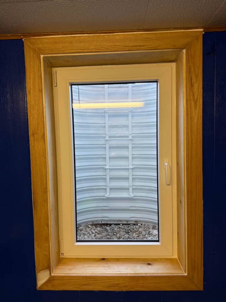 hite tilt and turn basement window with wood trim and a ladder visible in the well in Littleton, CO.