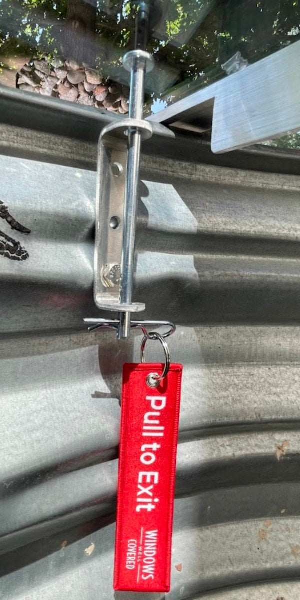 Window well cover lock with a red pull-to-exit release tag on a steel window well.