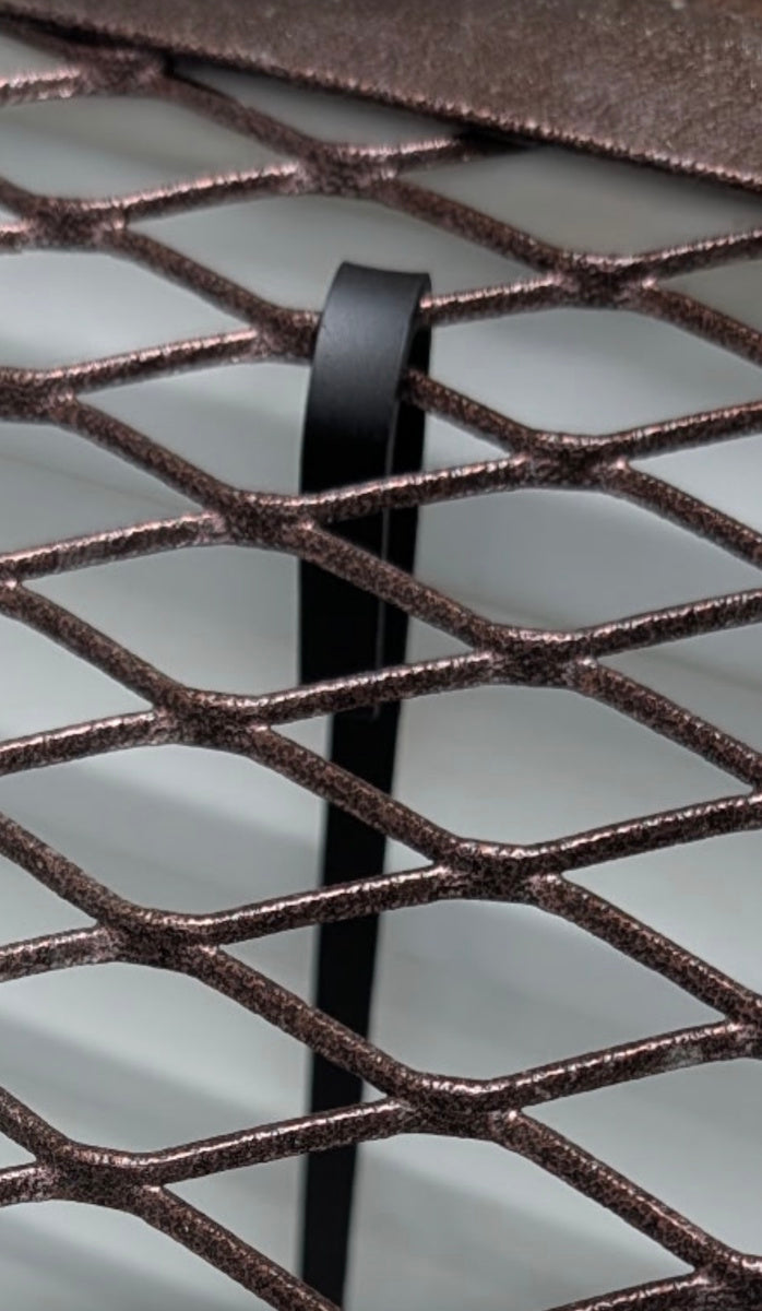 Black hook-bar lock holding a brown mesh window well grate in place.